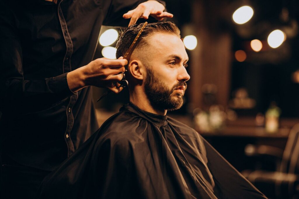 Barbier schneidet mit Schere und Kamm einen Undercut bei einem Kunden im Salon.